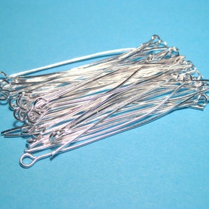May include: A pile of silver-toned head pins with a loop at one end. The pins are arranged in a random pattern and are all the same size.