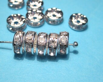May include: A close-up of a silver metal bead with clear rhinestones. The bead is on a blue surface and there are other beads in the background.