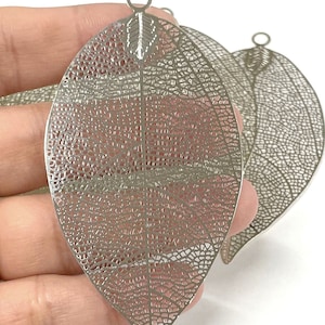 May include: Two silver metal leaf charms with a delicate, intricate design. The leaves have a hole at the top for hanging.