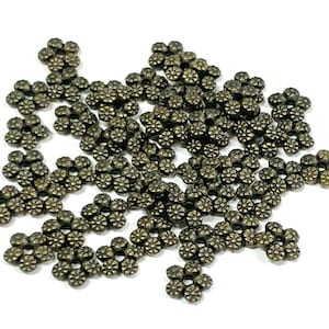 May include: A large pile of antique gold metal flower-shaped beads. The beads are all the same size and shape, and they are arranged in a random pattern.