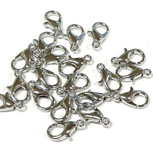 May include: A pile of silver-toned lobster clasps, a type of fastener used in jewelry making.