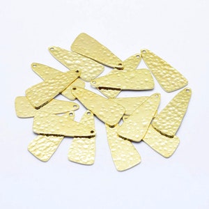 May include: A pile of gold-colored metal triangle-shaped charms with a hammered texture. Each charm has two small holes at the top.