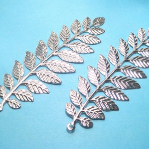 May include: Two silver metal leaf sprigs with a textured finish. Each sprig has a loop at the bottom for attaching to a project.