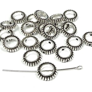 May include: A collection of silver-toned metal spacer beads with a ribbed, circular design and a central hole. One bead is threaded onto a thin silver-toned metal headpin with a small loop at one end, while the others are scattered loosely.