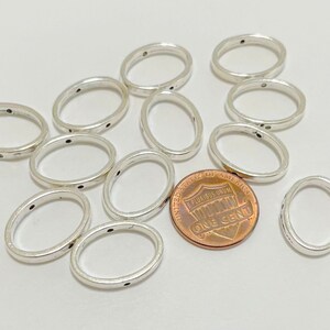 May include: A group of 10 silver oval-shaped jump rings with a dotted pattern. The rings are approximately the size of a US penny.