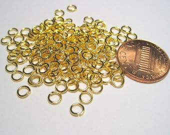May include: A large pile of gold jump rings, about the size of a US penny, on a white background.