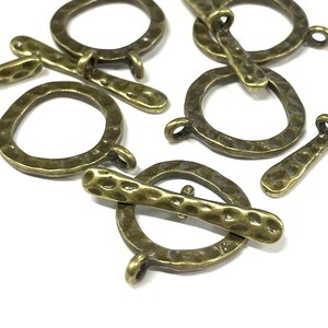 May include: A set of antique gold-toned metal toggle clasps with a hammered texture. The clasps are designed with a round loop and a straight bar.