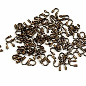 May include: A large quantity of antique gold-toned metal crimp beads. The beads are shaped like a small hook with a loop at the end.