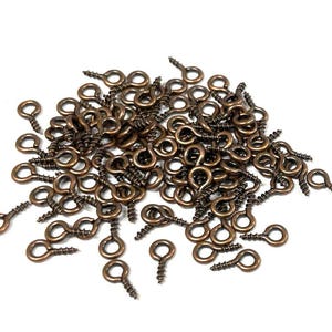 May include: A large pile of antique brass screw-in eye hooks. The hooks are all the same size and have a shiny finish.
