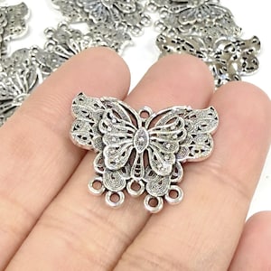 May include: Silver-toned butterfly-shaped charms with intricate filigree details. The charms have a central butterfly design with detailed wings and a series of small loops at the bottom. These charms are ideal for jewelry making and crafting.