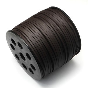 May include: A spool of dark brown flat leather cord. The cord is tightly wound around a black plastic spool with multiple circular holes. The leather appears to have a slightly textured surface.