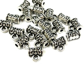 May include: A close-up of a pile of silver-toned metal end caps for jewelry making. The end caps have a decorative, ornate design and a small loop on the bottom.