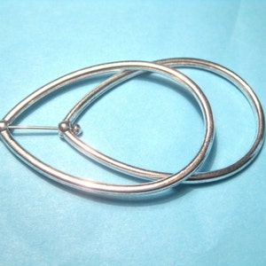 May include: A pair of silver-colored teardrop-shaped earrings. Each earring has a smooth, rounded design with a small ball at the top where the post connects. The earrings are displayed against a light blue background.