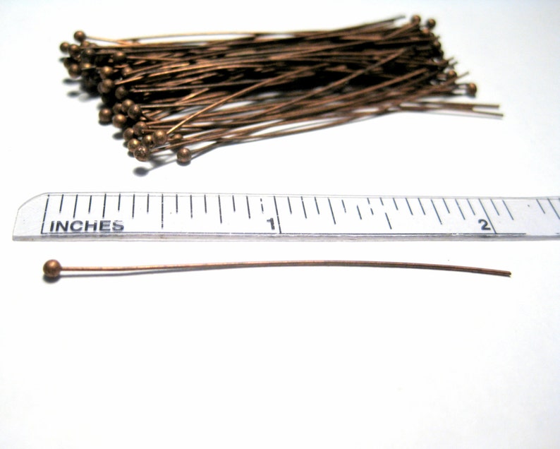 Puede incluir: Un mont&oacute;n de 100 alfileres de cabeza dorada, cada uno de 2,5 cm de largo. Los alfileres est&aacute;n dispuestos en un mont&oacute;n suelto sobre una superficie blanca. Una regla se coloca debajo del mont&oacute;n de alfileres para mostrar el tama&ntilde;o de los alfileres.