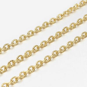 May include: Close-up of three gold-coloured chain strands. Each chain link has a textured, oval design. The chains are arranged diagonally against a white background, creating a pattern. The chains are likely for jewellery making.