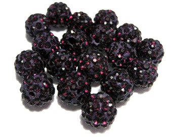 May include: A collection of round, spherical beads featuring a dark purple base covered in numerous small, reflective black crystals. Each bead has a textured, multi-faceted surface that catches the light, creating a shimmering appearance across the group.