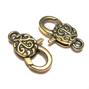 May include: Two gold-toned metal clasps with ornate swirl designs. Each clasp has a hook and a loop for attaching to a chain or cord.