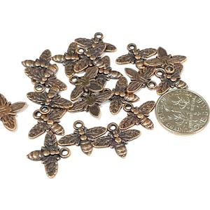 May include: A collection of 17 copper-toned metal bee charms with intricate details. Each charm features a stylized bee with wings, a body, and a head. The charms are perfect for adding a touch of whimsy to jewelry, crafts, and other projects.