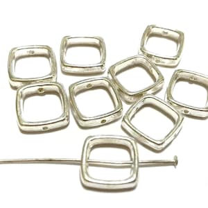 May include: A set of eight silver-toned metal square-shaped jump rings. The rings are open and have a smooth finish. The rings are approximately 1 inch in diameter.