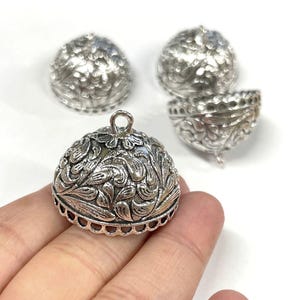 May include: Four silver metal dome-shaped embellishments with intricate floral designs. The embellishments have a small loop at the top for hanging.
