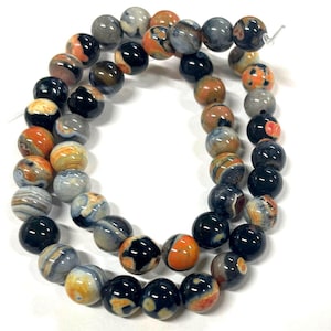 May include: Strand of round gemstone beads in shades of black, orange, gray, and cream. The beads have a polished, glossy finish and are strung together. Ideal for jewelry making.