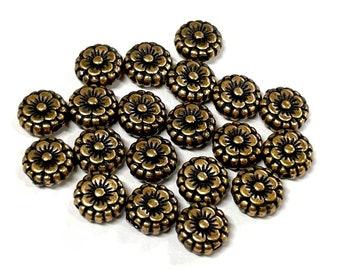 May include: A collection of small, bronze-colored, flower-shaped beads. Each bead has a detailed floral design with multiple petals and a central circular element. The beads are scattered on a white background.