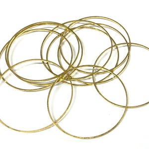 May include: A set of gold-colored metal bangles, stacked and intertwined. The bangles are smooth and shiny, with a circular shape.