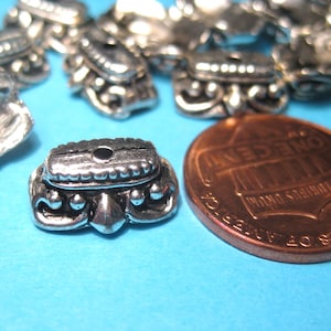 Peut inclure: Gros plan d'une perle en métal argenté avec un motif décoratif. La perle est à peu près de la taille d'une pièce de 1 centime d'euro.