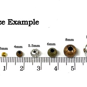 May include: Size example of round metal beads in various sizes from 2mm to 10mm. The beads are shown on a ruler with markings in millimeters.