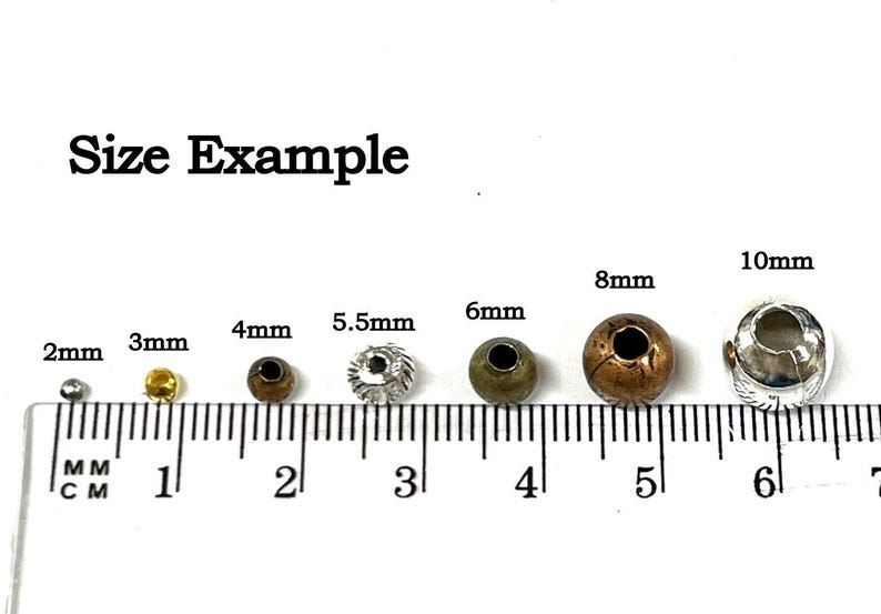 May include: Size example of round metal beads in various sizes from 2mm to 10mm. The beads are shown on a ruler with markings in millimeters.