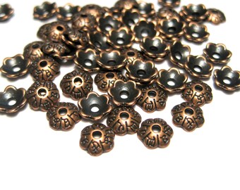 Puede incluir: Un montón de tapas de cuentas de metal de color cobre con acentos negros y diseños intrincados en forma de flor.