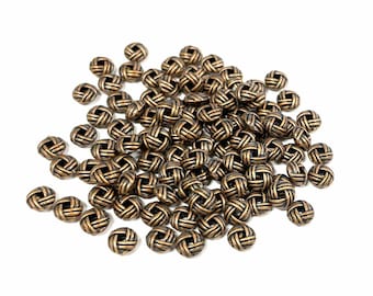May include: A large pile of small, round, gold-colored metal buttons with a woven design. The buttons are scattered on a white background.