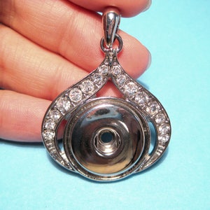 May include: Silver pendant with a clear crystal embellishment around the edge. The pendant has a round, silver-toned center with a small hole in the middle.