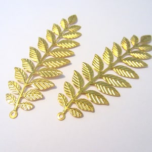 Pode incluir: Duas hastes de folhas de metal dourado com acabamento texturizado. Cada haste tem um laço na parte inferior para fixar.