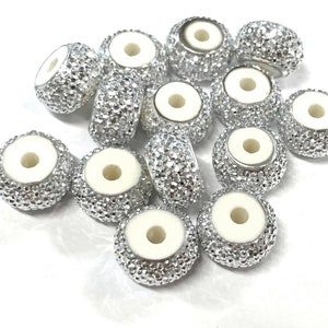 May include: A group of 12 silver beads with a white center hole. The beads are round and have a textured surface.