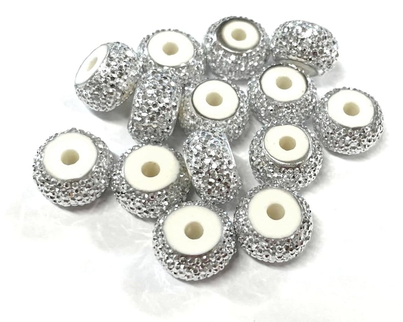 May include: A group of 12 silver beads with a white center hole. The beads are round and have a textured surface.