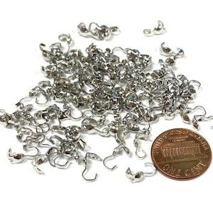 May include: A large pile of silver-toned metal clasps, some with a rounded ball at the end, next to a US penny.