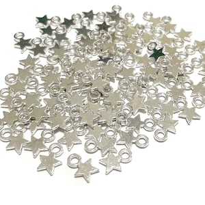 May include: A large pile of silver star-shaped charms with a jump ring attached to each star. The charms are scattered on a white background.