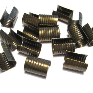 May include: A group of 15 antique gold metal crimp ends for jewelry making. The crimp ends are ribbed and have a slightly curved shape.