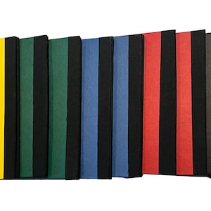 May include: A collection of colorful notebooks with black spines and elastic closures. The notebooks are in various colors, including yellow, green, blue, red, and gray. The notebooks are arranged in a row, with the yellow notebook in the front.