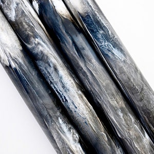 May include: Close-up of several cylindrical objects with a marbled appearance. The cylinders are primarily shades of gray and black, with white marbling throughout. The objects are arranged diagonally against a white background.