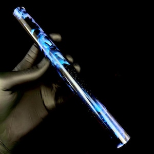 May include: A clear, cylindrical object with a swirling blue and white design. The object is held against a black background, showcasing its translucent qualities and artistic pattern. The design resembles a galaxy.