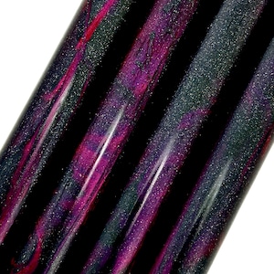 May include: Close-up of four black and pink marbled pens with a glittery finish.