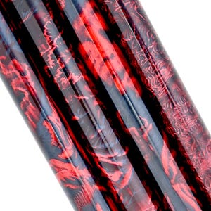May include: Close-up of a cylindrical object with a striking red and black marbled pattern. The design features swirling, organic shapes and vertical black stripes, creating a visually dynamic effect. The surface appears glossy.