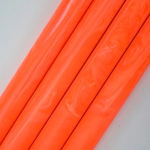 Puede incluir: Cuatro varillas de acrílico marmoleadas de color naranja y blanco. Las varillas están dispuestas en diagonal, con el marmoleado blanco creando un efecto de remolino.