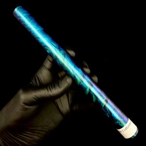 以下が含まれることがあります： 青、ティール、紫の色合いが渦巻く模様の円筒形の物体。黒い背景に対して、手袋をはめた手で物体が保持されています。物体には「Craftsman」と書かれたラベルが付いています。