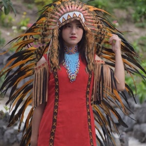 Peut inclure: Une femme portant une robe rouge avec des bordures brunes et noires et un collier de perles. Elle porte une grande coiffe avec des plumes noires et jaunes.