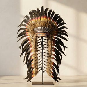 May include: A decorative feathered headdress featuring long black feathers with yellow and red tips, arranged in a circular fan shape. The center band displays intricate beadwork in white, blue, and orange patterns, accented by brown fur trim.