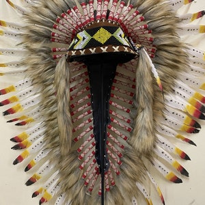 May include: A Native American headdress with white and brown feathers, red and white wrappings, and a beaded headband with black, white, and yellow accents.