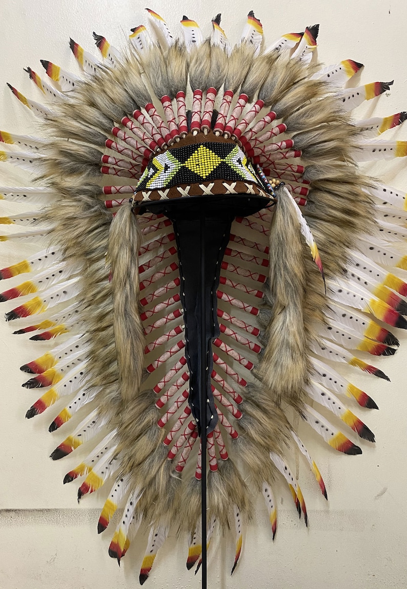 May include: A Native American headdress with white and brown feathers, red and white wrappings, and a beaded headband with black, white, and yellow accents.